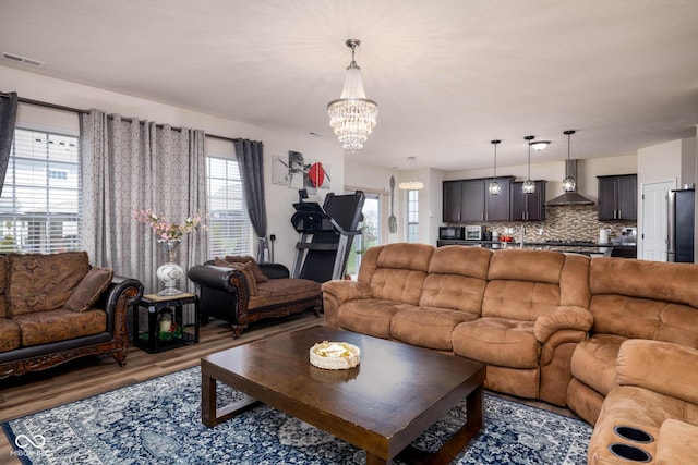 living room with an inviting chandelier, wood finished floors, visible vents, and a healthy amount of sunlight