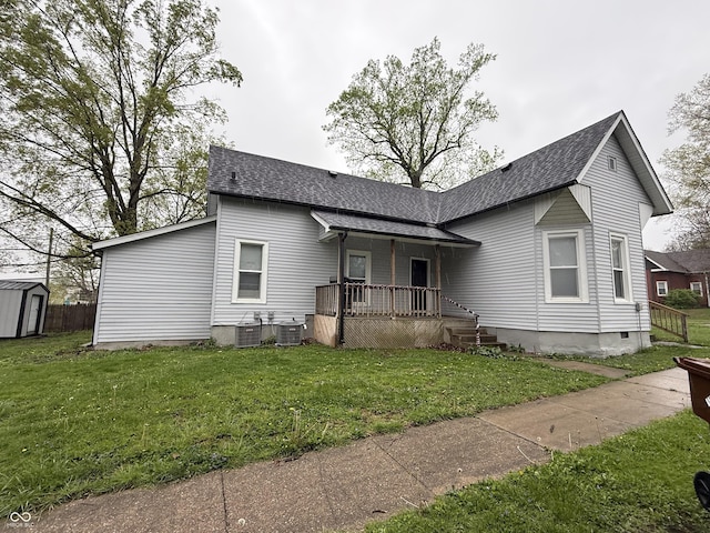 view of front facade featuring roof with shingles, central AC unit, a front yard, and a storage shed