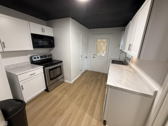 kitchen featuring light wood-style floors, a sink, white cabinetry, black microwave, and stainless steel range with electric stovetop