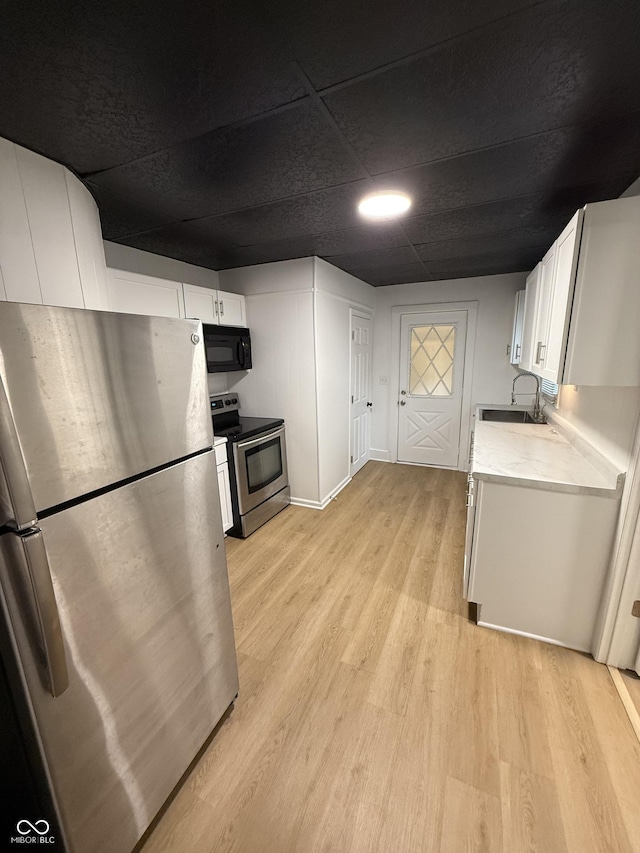 kitchen with white cabinets, a sink, stainless steel appliances, light countertops, and light wood finished floors