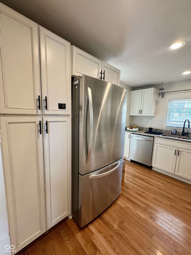 kitchen with white cabinetry, appliances with stainless steel finishes, a sink, and light wood-style floors