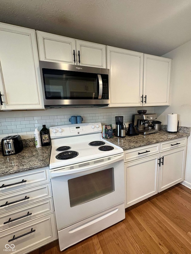 kitchen with stainless steel microwave, white range with electric stovetop, white cabinets, and tasteful backsplash