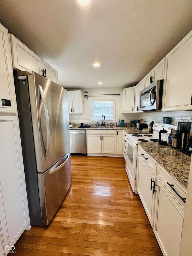 kitchen with appliances with stainless steel finishes, a sink, light wood-style flooring, white cabinetry, and tasteful backsplash