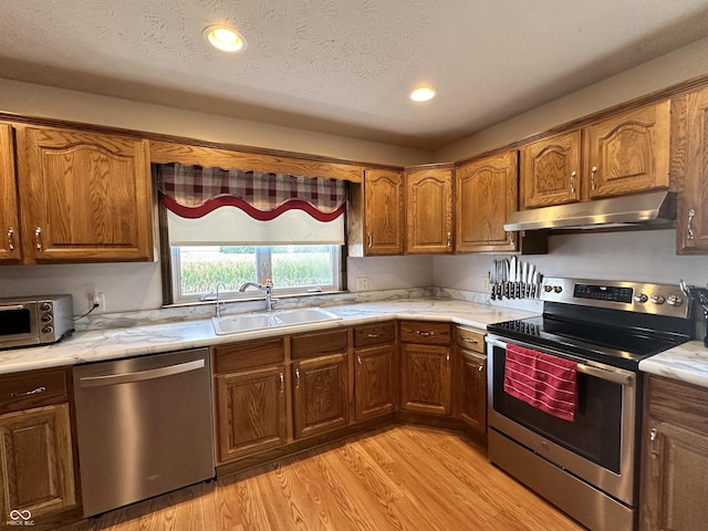 kitchen featuring a sink, recessed lighting, light wood-style floors, under cabinet range hood, and appliances with stainless steel finishes