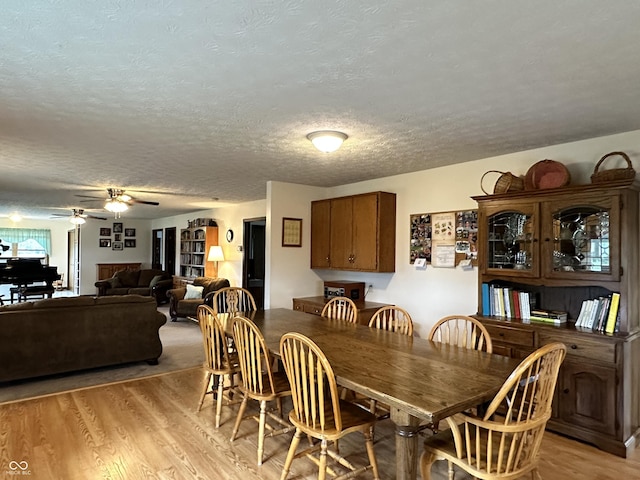 dining space with ceiling fan, light wood-style floors, and a textured ceiling