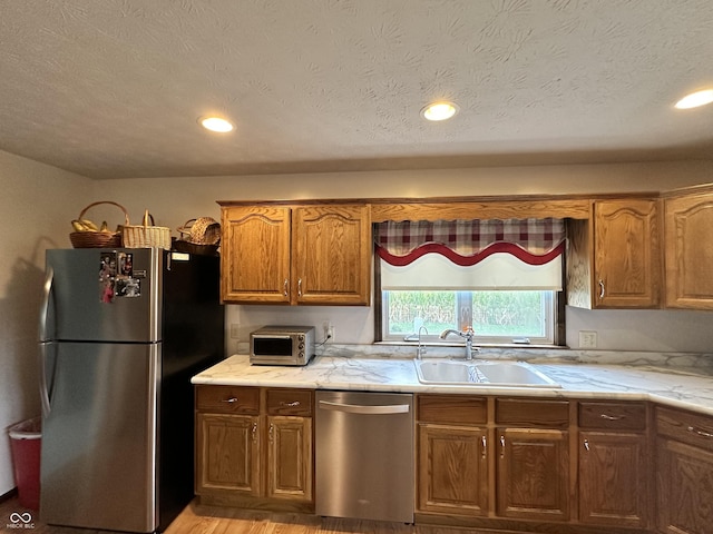 kitchen with brown cabinets, recessed lighting, light stone counters, a sink, and appliances with stainless steel finishes