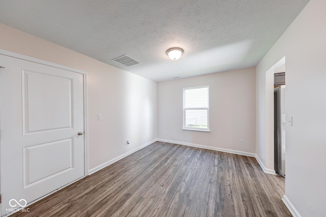 spare room featuring a textured ceiling, baseboards, visible vents, and dark wood-style floors