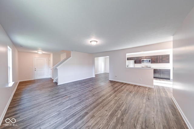unfurnished living room with baseboards, wood finished floors, and stairs