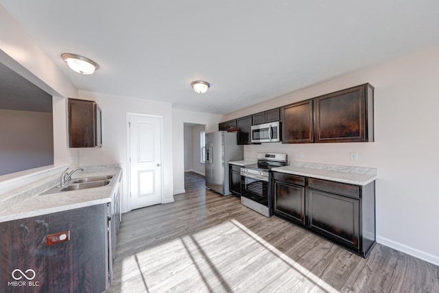 kitchen with dark brown cabinets, light wood-style flooring, stainless steel appliances, and a sink