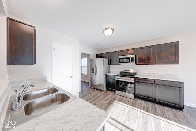 kitchen featuring light countertops, dark brown cabinets, a sink, light wood-style floors, and appliances with stainless steel finishes
