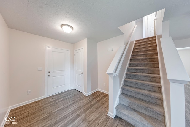 staircase with wood finished floors, a textured ceiling, and baseboards