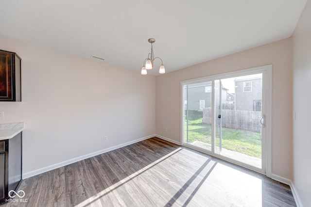 unfurnished dining area with visible vents, baseboards, wood finished floors, and an inviting chandelier