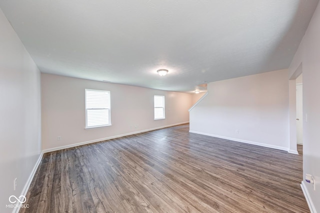 unfurnished living room featuring baseboards and dark wood-type flooring