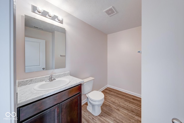 half bathroom featuring wood finished floors, visible vents, vanity, and toilet