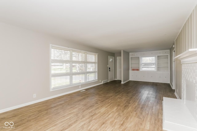 9535 E Michigan St, Indianapolis, IN 46229 - unfurnished living room featuring built in shelves, a brick fireplace, visible vents, baseboards, and wood finished floors