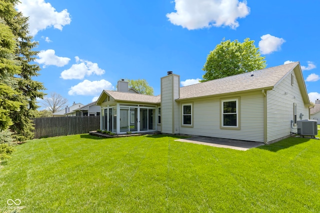 rear view of house with fence, a lawn, central AC unit, and a sunroom