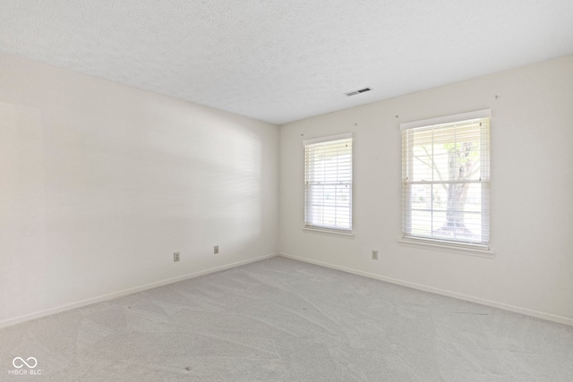 unfurnished room with visible vents, a textured ceiling, baseboards, and light carpet
