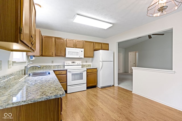 kitchen featuring a sink, brown cabinets, white appliances, and light wood-style flooring