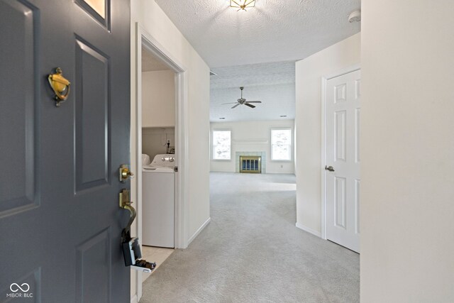 carpeted foyer featuring a tiled fireplace, a ceiling fan, a textured ceiling, and independent washer and dryer