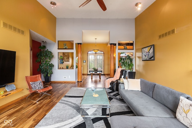 living room with wood finished floors, visible vents, a ceiling fan, and a towering ceiling