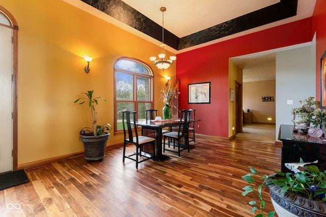 dining area featuring wood-type flooring, an inviting chandelier, a tray ceiling, and baseboards