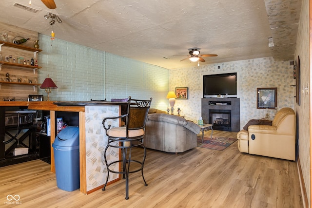 living room featuring a glass covered fireplace, wood finished floors, visible vents, and ceiling fan