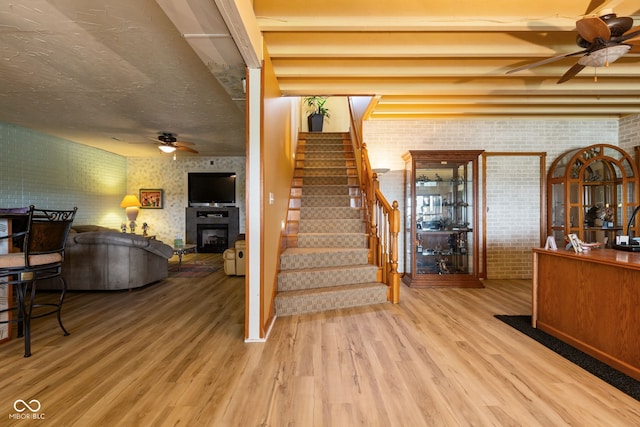 staircase with a glass covered fireplace, a ceiling fan, wood finished floors, and brick wall