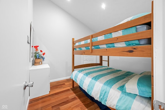 bedroom with baseboards, wood finished floors, and high vaulted ceiling