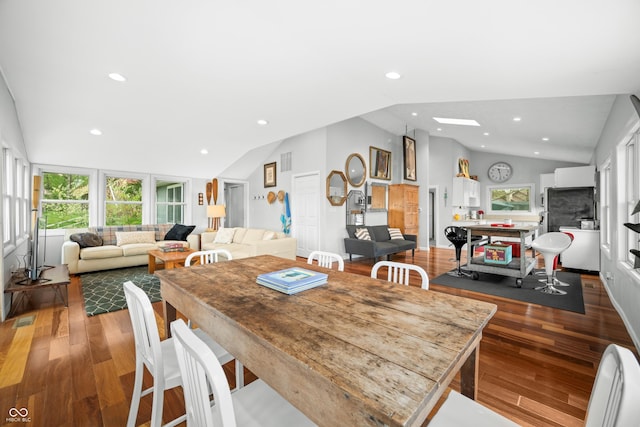 dining space featuring wood finished floors, vaulted ceiling with skylight, and a wealth of natural light