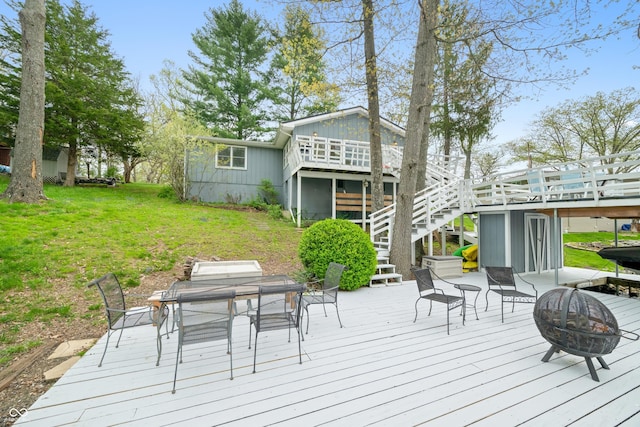 wooden terrace with outdoor dining area, a yard, a fire pit, and stairway