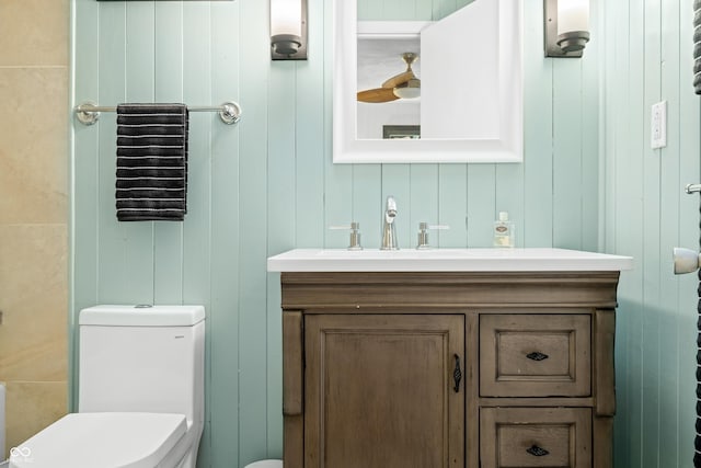 bathroom featuring toilet, wood walls, and vanity
