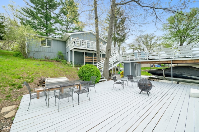 deck featuring a lawn, stairs, outdoor dining area, and a fire pit