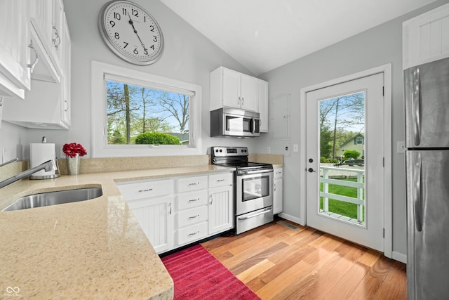 kitchen with white cabinets, a sink, light wood-style flooring, vaulted ceiling, and stainless steel appliances