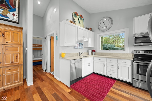 kitchen featuring white cabinets, stainless steel appliances, wood finished floors, and a towering ceiling
