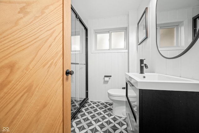 full bath with vanity, a decorative wall, toilet, and a shower stall