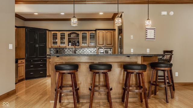 bar featuring crown molding, tasteful backsplash, light wood-style floors, and hanging light fixtures