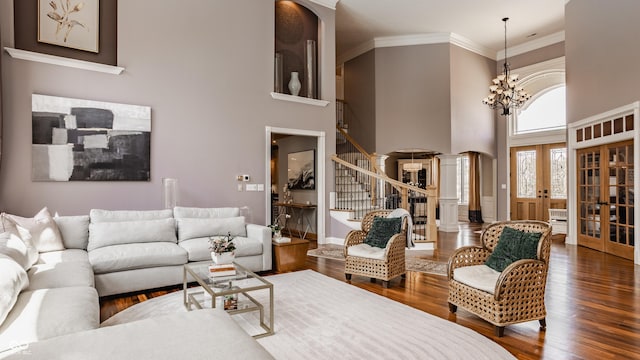 living room with wood finished floors, stairs, french doors, a towering ceiling, and ornate columns
