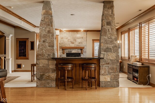 bar with crown molding, wood finished floors, a fireplace, baseboards, and ornate columns