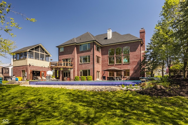 back of property featuring a chimney, brick siding, a lawn, a sunroom, and an outdoor pool