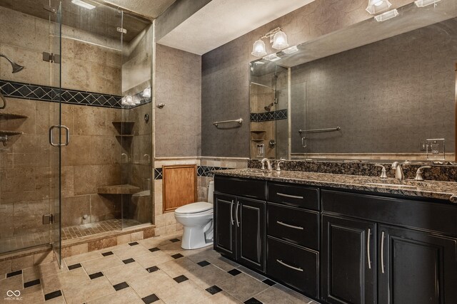 bathroom featuring a wainscoted wall, a sink, double vanity, a stall shower, and toilet