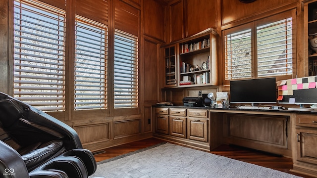 office with built in study area, wood walls, and dark wood-style flooring