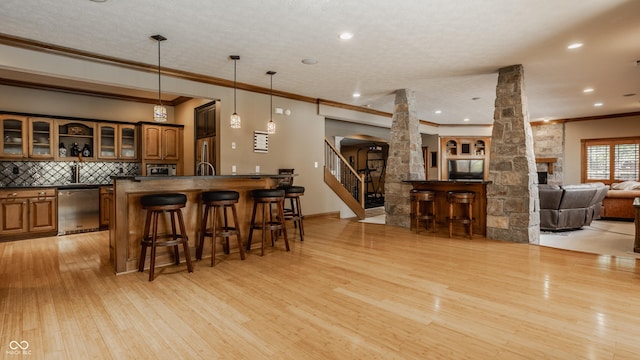 bar with wet bar, light wood-type flooring, decorative columns, appliances with stainless steel finishes, and ornamental molding