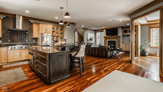 kitchen with wall chimney range hood, light brown cabinets, ornamental molding, and stainless steel appliances