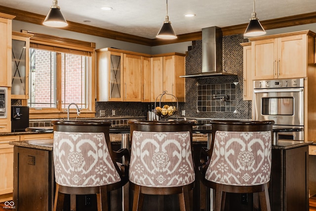 kitchen featuring light brown cabinetry, backsplash, ornamental molding, a kitchen island, and wall chimney exhaust hood