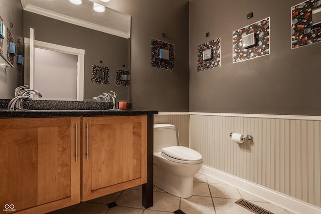 bathroom with a wainscoted wall, tile patterned floors, toilet, vanity, and crown molding