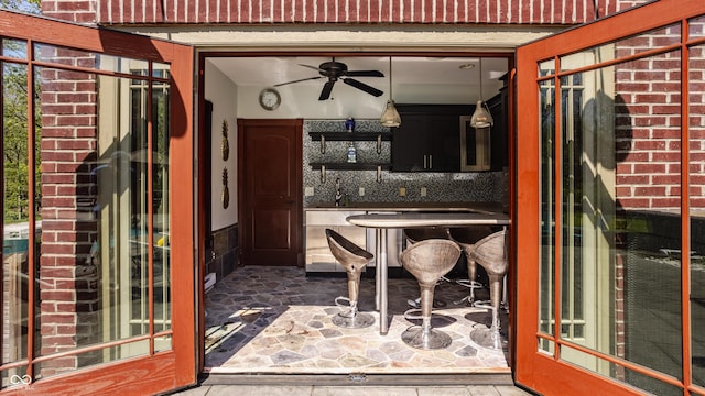 exterior space featuring open shelves, decorative backsplash, stone finish flooring, and ceiling fan