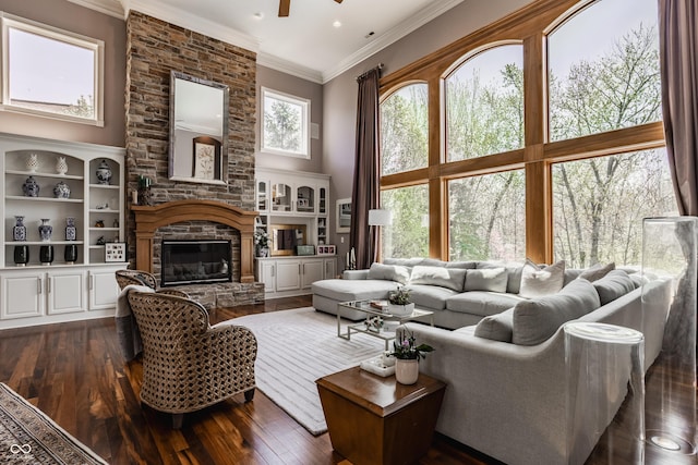 living area featuring dark wood finished floors, a ceiling fan, crown molding, and a fireplace