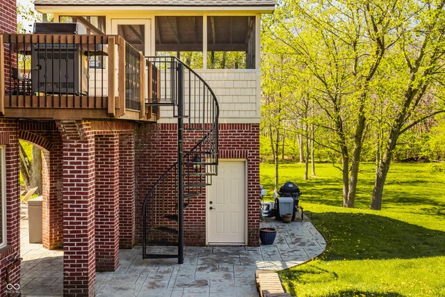 back of house featuring stairs, a yard, a patio area, brick siding, and a sunroom