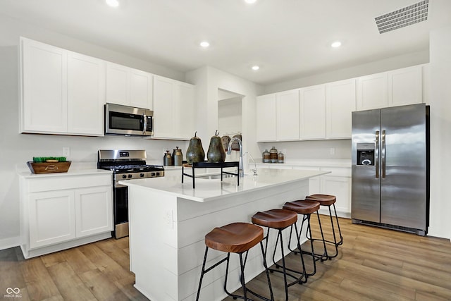 kitchen featuring a center island with sink, visible vents, stainless steel appliances, and light wood-style floors