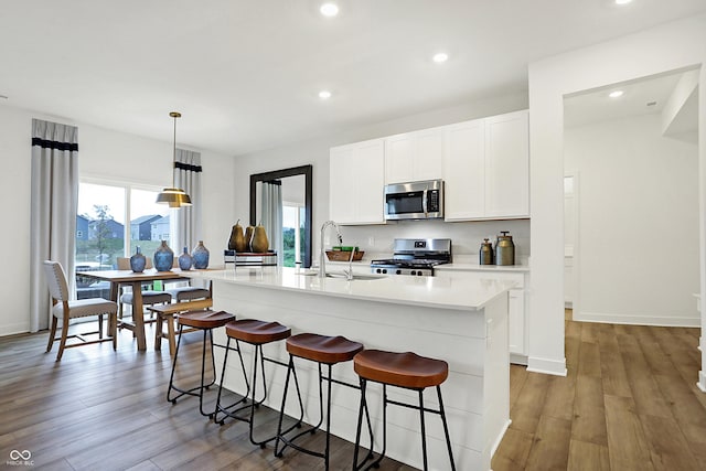 kitchen featuring a sink, a breakfast bar, stainless steel appliances, light countertops, and a center island with sink